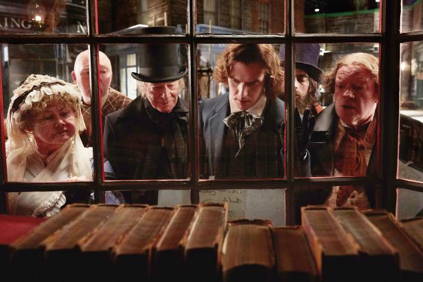 Mehrere Personen in historischer Kleidung schauen durch ein Schaufenster auf Bücher.