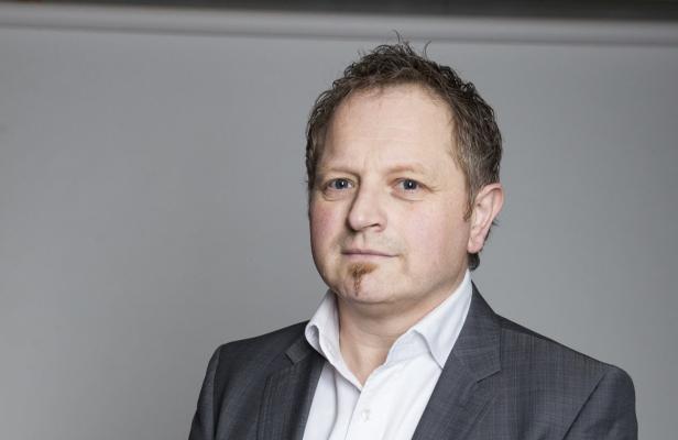 Gerald Reischl Porträt eines Mannes mit Anzug vor einem grauen Hintergrund.