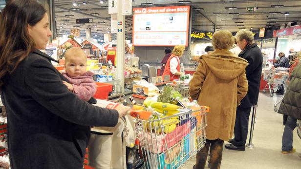 Eine Frau mit einem Baby im Arm steht an der Kasse eines Supermarktes.