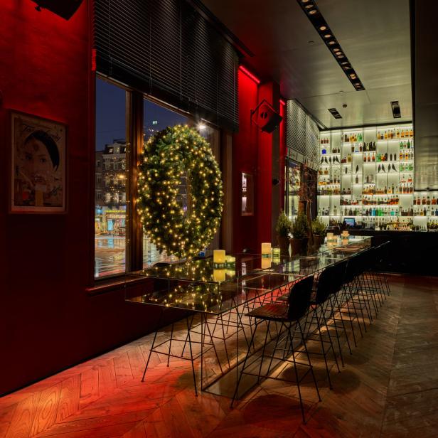 Ein langer Tisch mit Stühlen in einer Bar, dekoriert mit einem beleuchteten Weihnachtskranz.