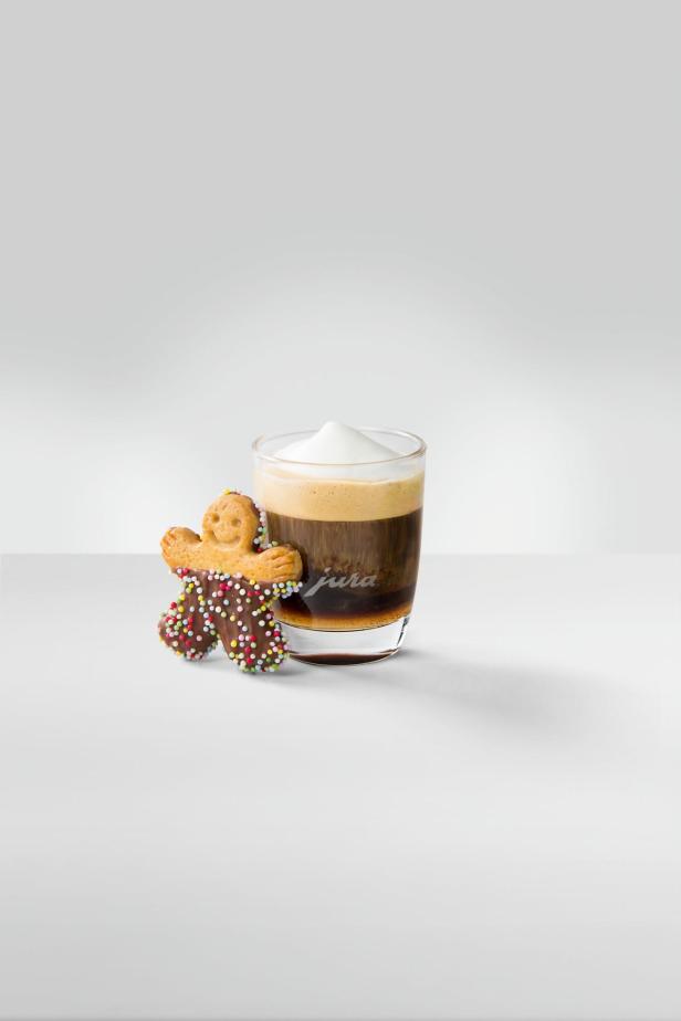 Ein Lebkuchenmann steht neben einem Glas Kaffee mit Milchschaum.