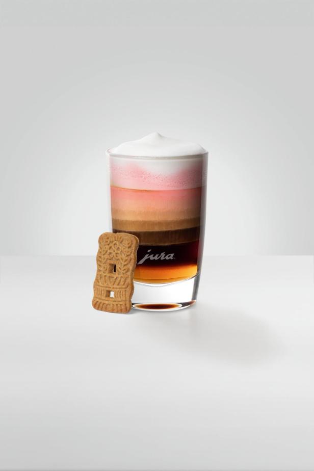 Ein Glas Latte Macchiato mit einem Keks der Marke Jura daneben.