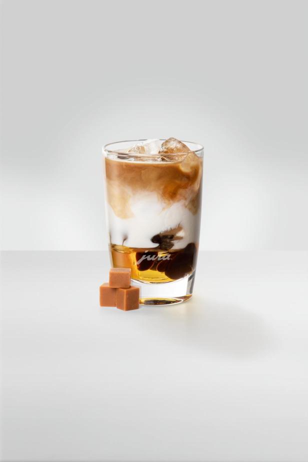 Ein Glas mit Eiskaffee und Karamellwürfeln auf einem Tisch.