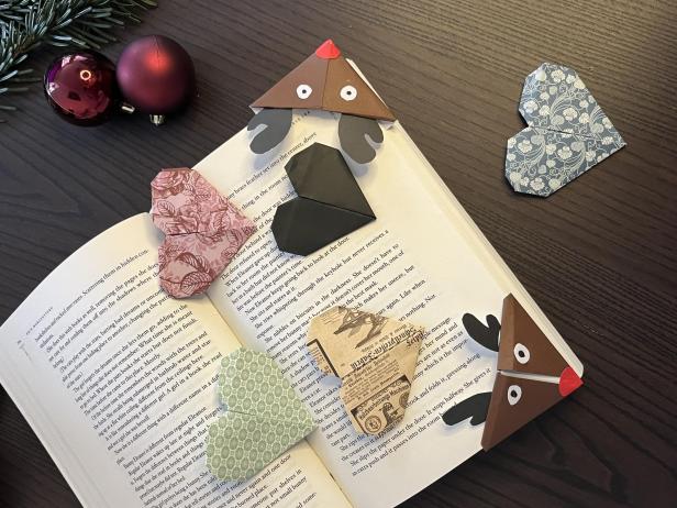 Ein aufgeschlagenes Buch mit mehreren Origami-Lesezeichen und zwei Weihnachtskugeln im Hintergrund.