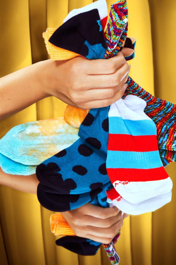 Zwei Hände halten einen Stapel bunter Socken vor einem goldenen Hintergrund.