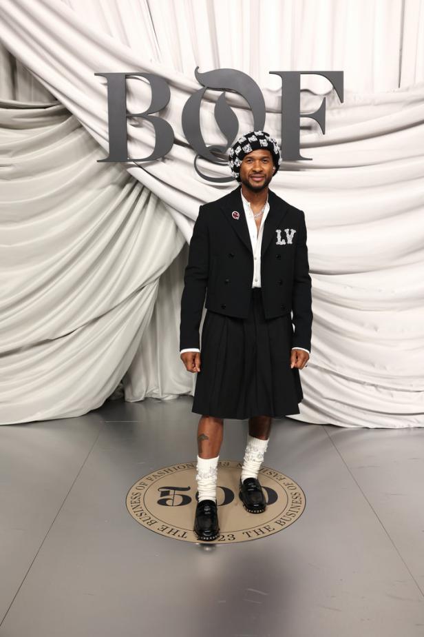 Usher posiert vor einem „BoF 500“-Hintergrund in einem schwarzen Rock und einer passenden Jacke.