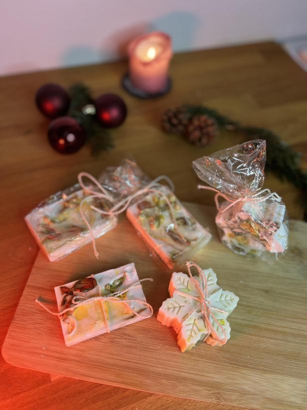 Weihnachtliche Seifenstücke, teilweise verpackt, liegen auf einem Holzbrett.