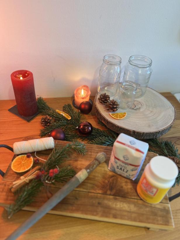 Dekorationen und Materialien für winterliches Basteln mit Kerzen und Gläsern auf einem Tisch.