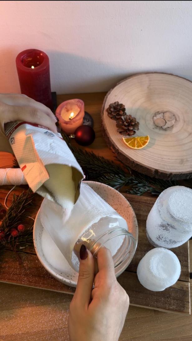 Eine Person schüttet Zucker in ein Glas, um es weihnachtlich zu dekorieren.