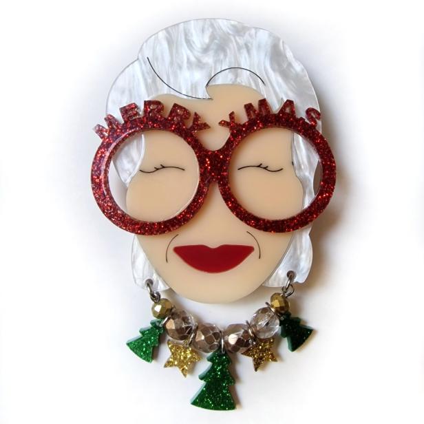 Eine stilisierte Brosche zeigt ein Gesicht mit einer „Merry Xmas“-Brille und Weihnachtsschmuck.