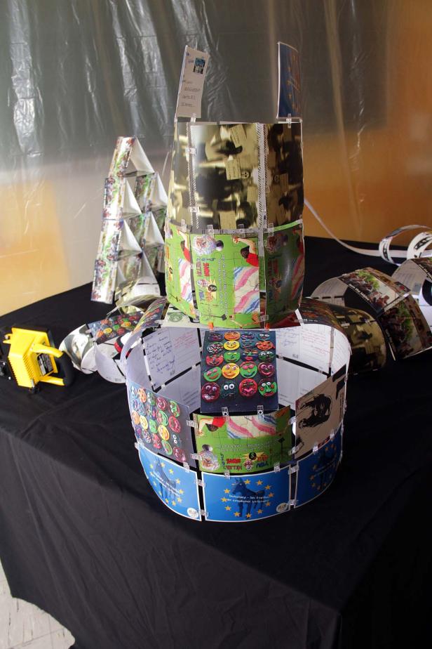 Eine Turm-Skulptur aus Puzzleteilen und Postkarten auf einem Tisch.