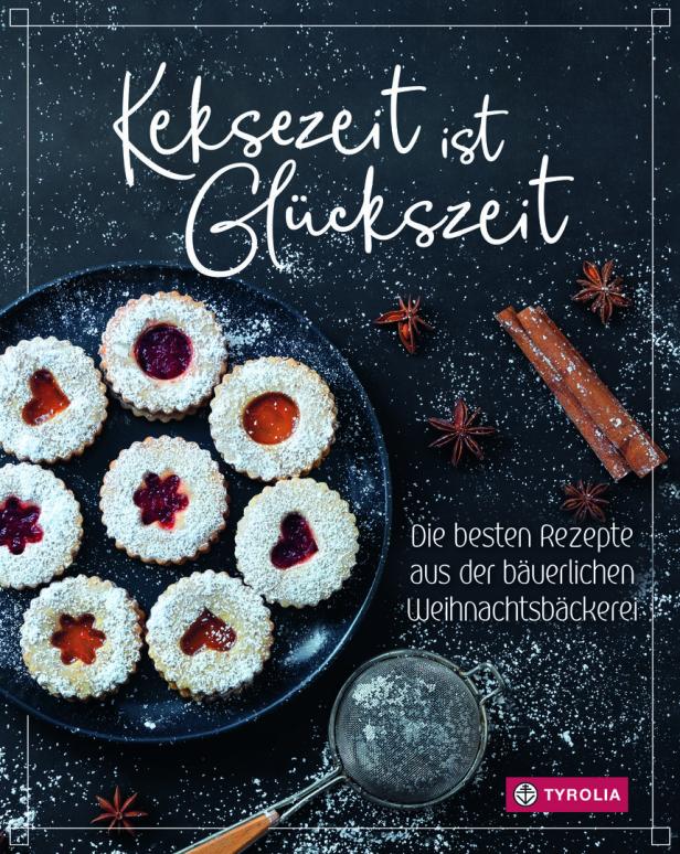 Ein Teller mit Weihnachtsplätzchen, bestäubt mit Puderzucker, umgeben von Zimtstangen und Sternanis.