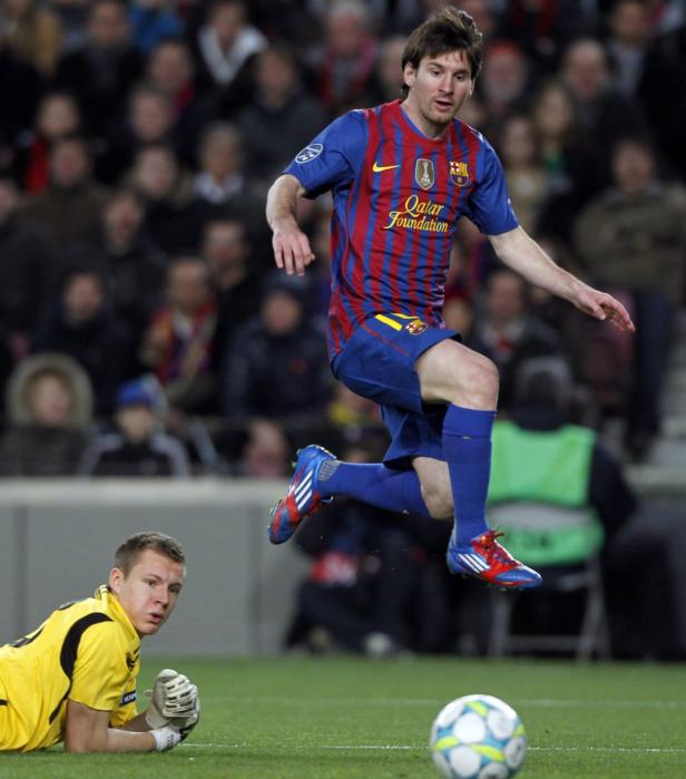 Lionel Messi springt über einen Ball, während ein Torwart am Boden liegt.