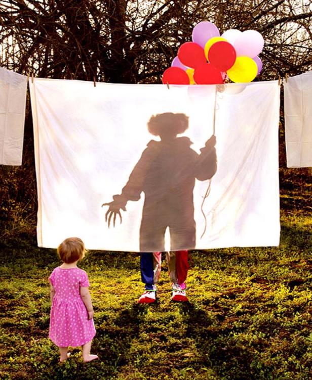 Ein Mädchen blickt auf den Schatten eines Clowns mit Ballons, der hinter einem Tuch steht.