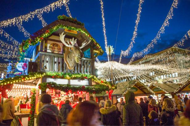 Ein belebter Weihnachtsmarkt mit festlich geschmückten Ständen und Lichtern.