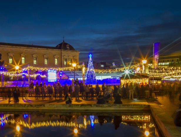 Ein Weihnachtsmarkt mit Menschen und einem beleuchteten Weihnachtsbaum bei Nacht.