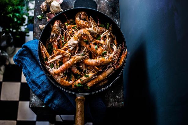 Gegrillte Scampi mit Knoblauch und Petersilie in einer schwarzen Pfanne angerichtet.