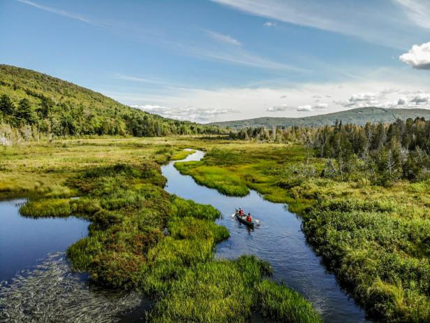 Zwei Personen paddeln in einem Kanu auf einem Fluss durch eine grüne Landschaft.