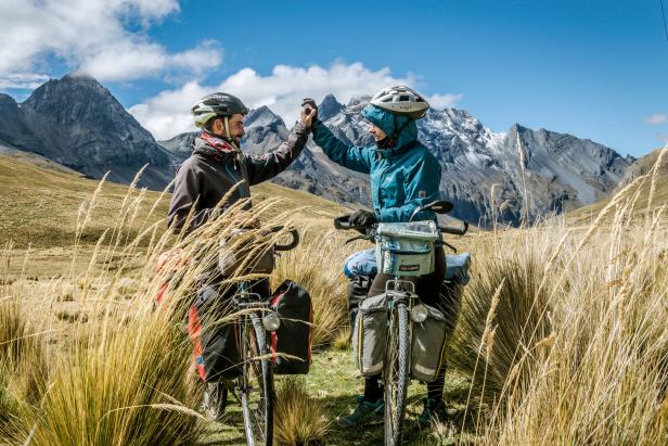 Zwei Radfahrer geben sich vor einer Bergkulisse ein High-Five.