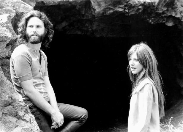 Ein Schwarzweißfoto von Jim Morrison und einer jungen Frau vor einer dunklen Höhle.