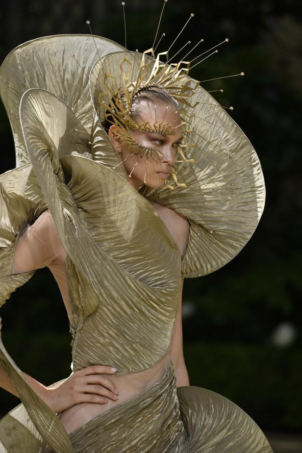 Ein Model präsentiert ein extravagantes goldenes Kleid und einen Kopfschmuck.