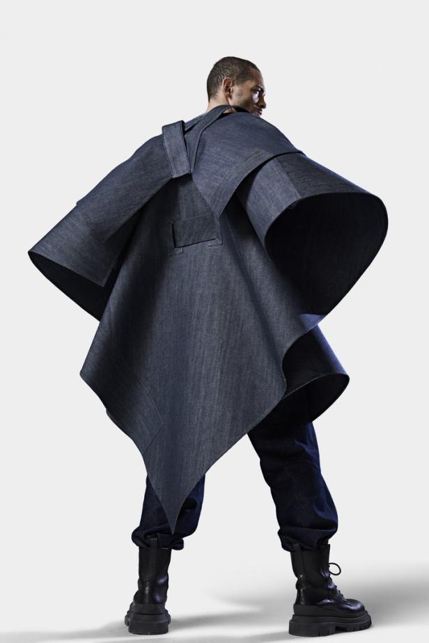 Ein Mann trägt einen übergroßen Denim-Poncho und Stiefel.