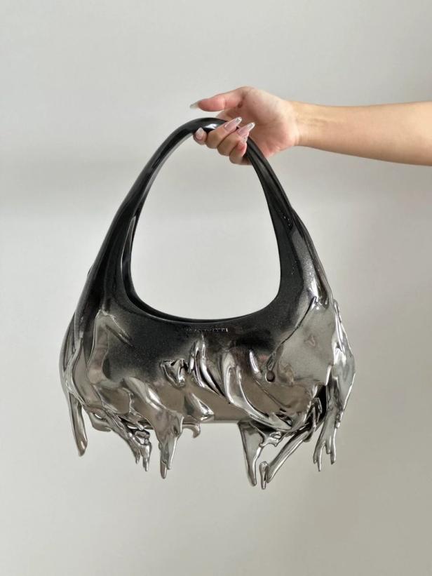 Eine Hand hält eine glänzende, silberfarbene Handtasche mit tropfenförmigen Verzierungen.