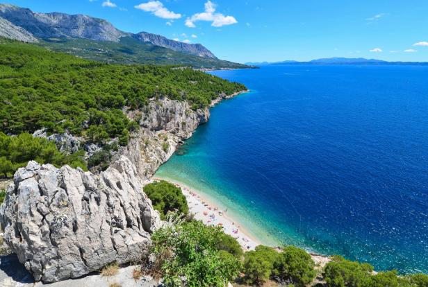 Ein Panoramablick auf einen Strand mit türkisfarbenem Wasser und bewaldeten Klippen.