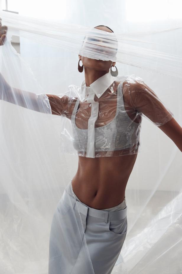 Eine Frau posiert in einem transparenten Hemd und einer Hose, teilweise von Plastik verdeckt.
