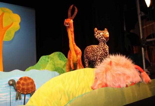 Eine Puppenspielszene mit einer Giraffe, einem Leoparden, einem Monster und einer Schildkröte.
