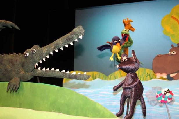 Ein Krokodil, ein Vogel, ein Erdmännchen, eine Schlange, eine Giraffe und ein Nilpferd auf einer Bühne.