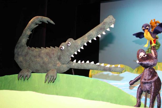 Ein Krokodil mit offenem Maul und weitere Stofftiere auf einer Bühne.