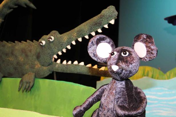 Eine Stoffmaus steht vor einem Krokodil mit geöffnetem Maul.