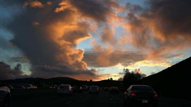 Autos fahren auf einer Autobahn unter einem dramatischen, orangefarbenen Himmel.