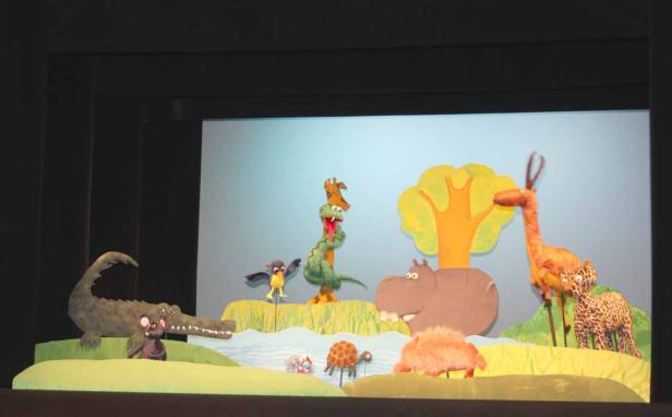 Eine Bühne mit handgemachten Tierfiguren vor einem hellblauen Hintergrund.