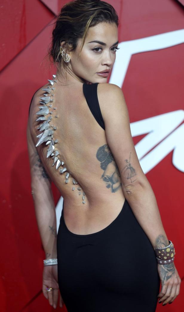 Rita Ora mit einem schwarzen Kleid und einem Schmuckstück, das wie eine Wirbelsäule aussieht.