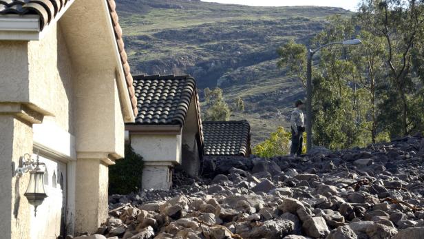 Ein Haus ist von einer Gerölllawine getroffen worden; ein Mann steht daneben.