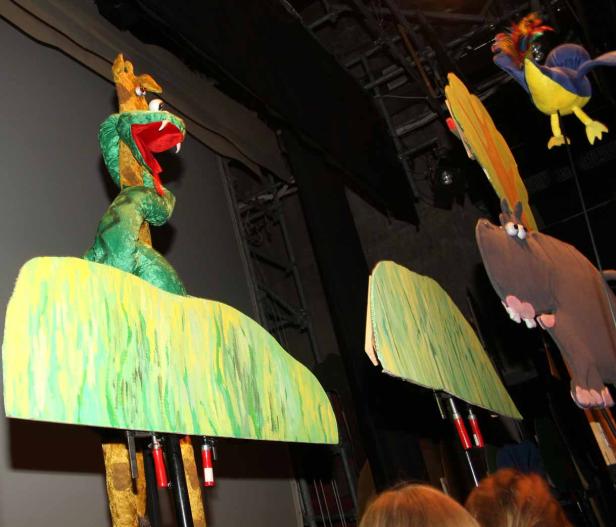 Puppen einer Schlange, eines Nilpferds und eines Vogels auf einer Bühne.