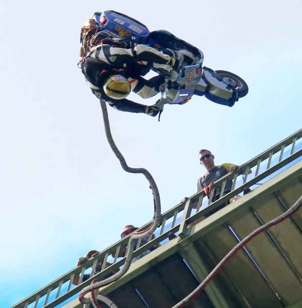 Ein Motorradfahrer springt mit einem Bungee-Seil von einer Brücke.