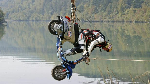 Ein Mann hängt mit einem Motorroller an einem Seil über einem See.