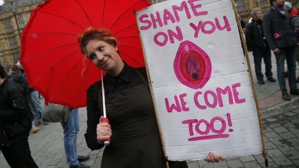Eine Frau mit rotem Regenschirm hält ein Schild mit der Aufschrift „Shame on you, we come too!".
