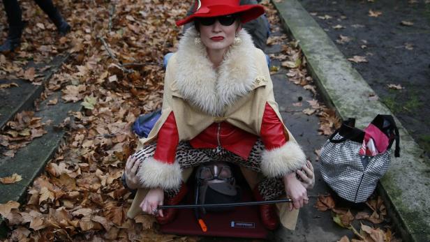 Eine Frau in auffälliger Kleidung reitet auf dem Rücken einer Person in einem Park voller Herbstlaub.