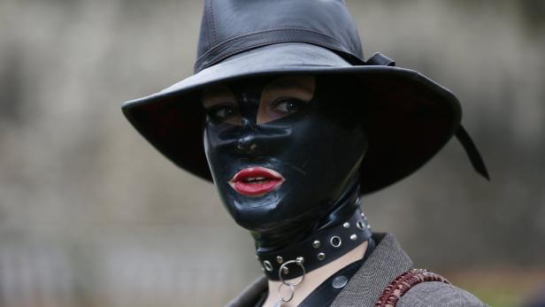 Eine Person mit Lackmaske, Hut und Halsband blickt in die Kamera.