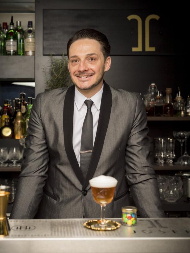 Philipp M. Ernst steht hinter einer Bar mit einem Cocktail.