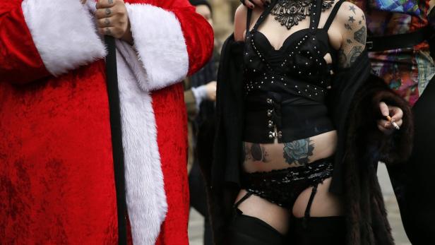 Ein Weihnachtsmann steht neben einer tätowierten Frau in Dessous, die eine Zigarette raucht.