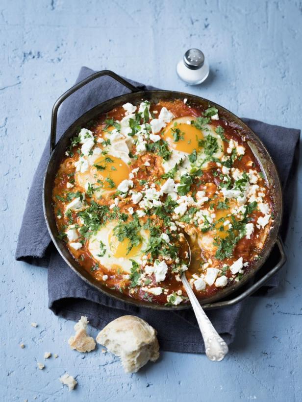 Shakshuka mit Eiern, Tomaten, Feta und Petersilie in einer Pfanne serviert.