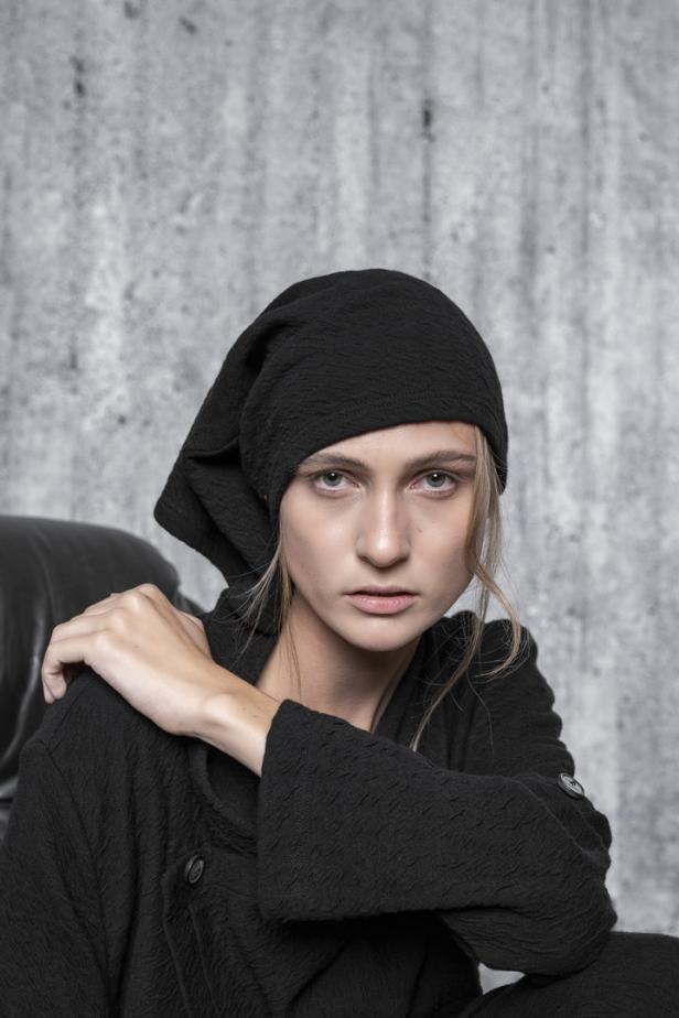 Eine Frau mit einem schwarzen Turban und einem passenden Oberteil vor einem grauen Hintergrund.