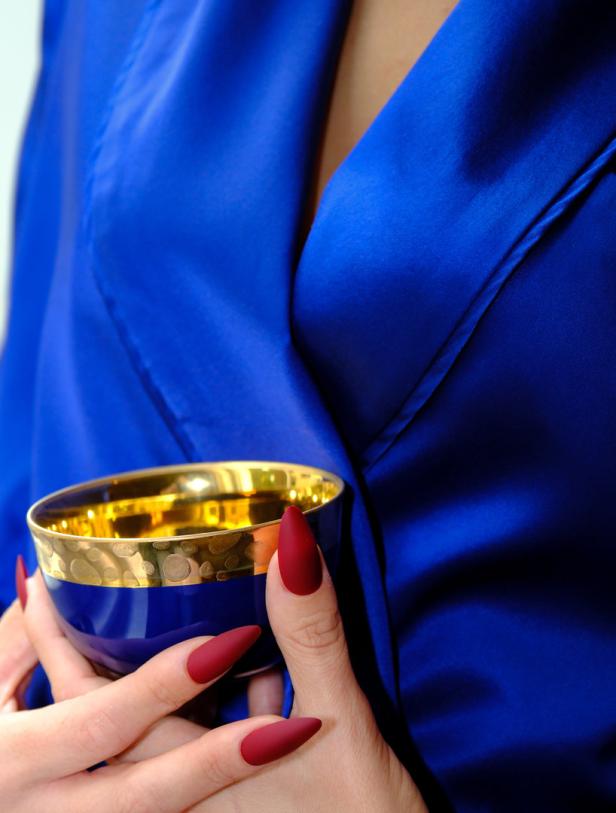 Eine Frau im blauen Seidenmantel hält eine blau-goldene Schale in den Händen.