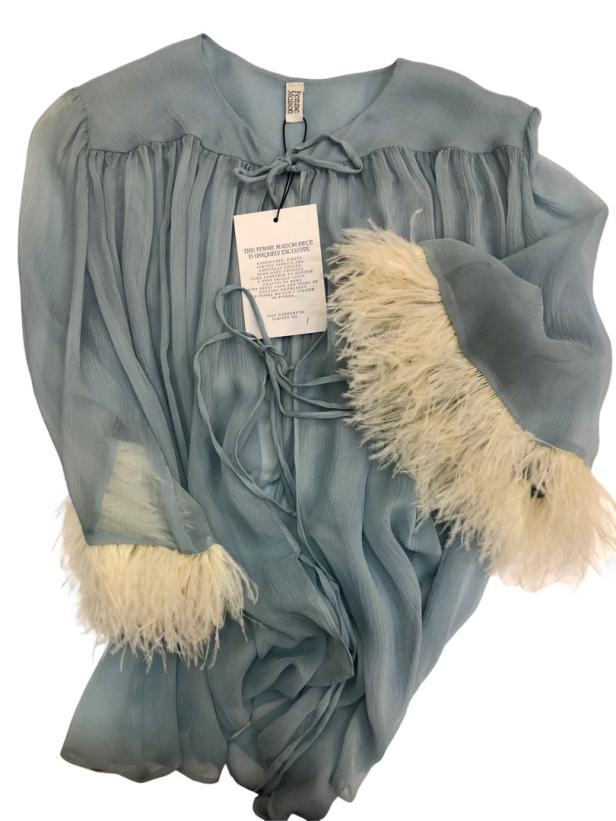 Eine hellblaue Chiffonbluse mit langen Ärmeln und weißen Federbesätzen an den Manschetten.