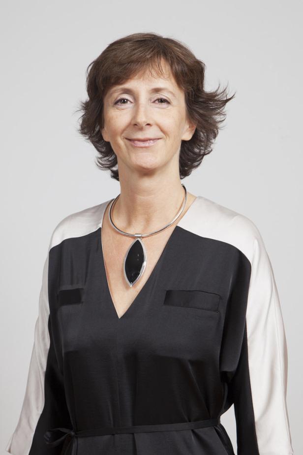Eine Frau mit braunen Haaren und einer Halskette mit einem großen, schwarzen Anhänger lächelt.
